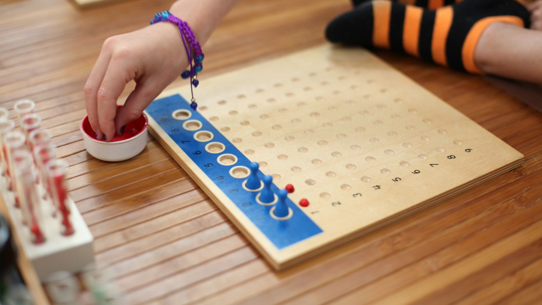 Close up of a rectangular board with 100 indentations in a 10 by 10 grid with beads and placeholders