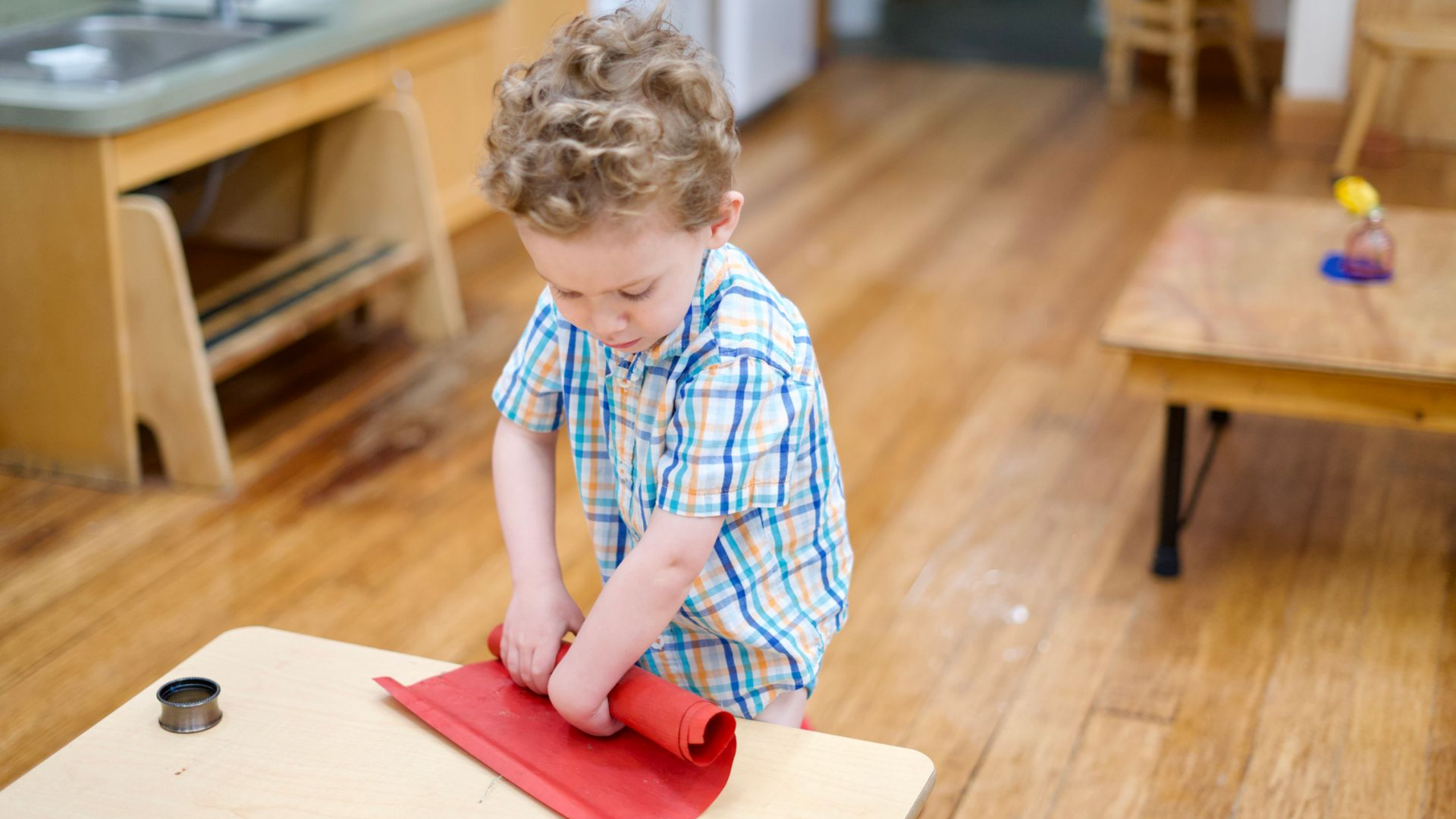 image of a preschool aged boy standing behind a low table rolling up a placemat