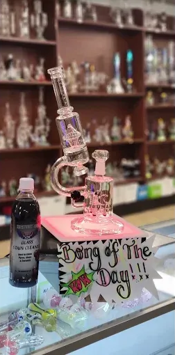 Pink glass bong display on a counter with a “King of the Day” sign in a shop.