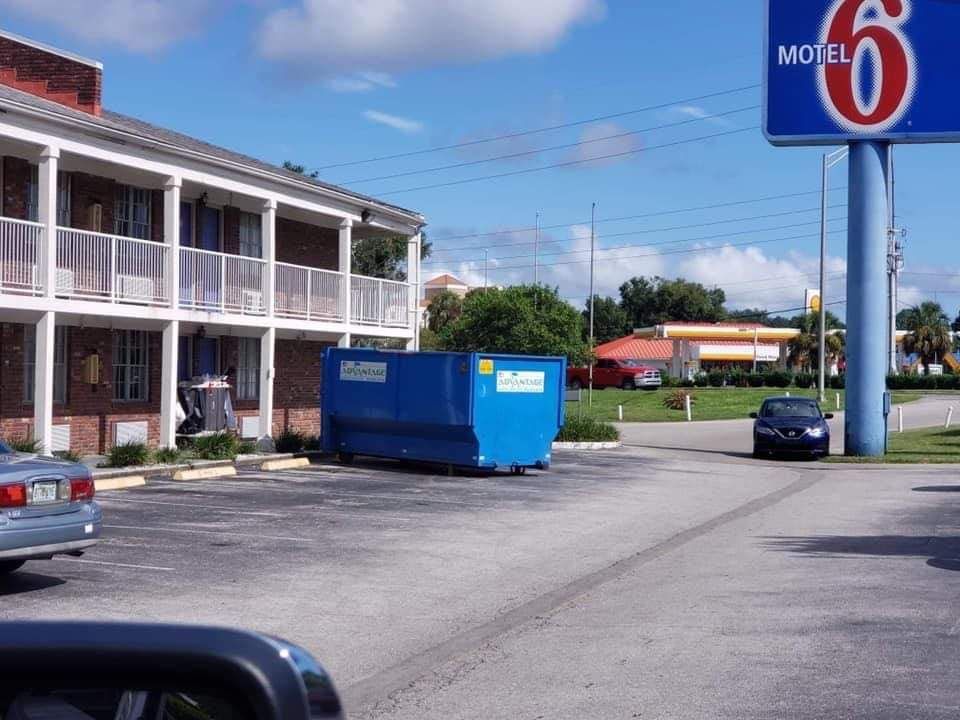 A blue dumpster is parked in front of a motel 6 sign