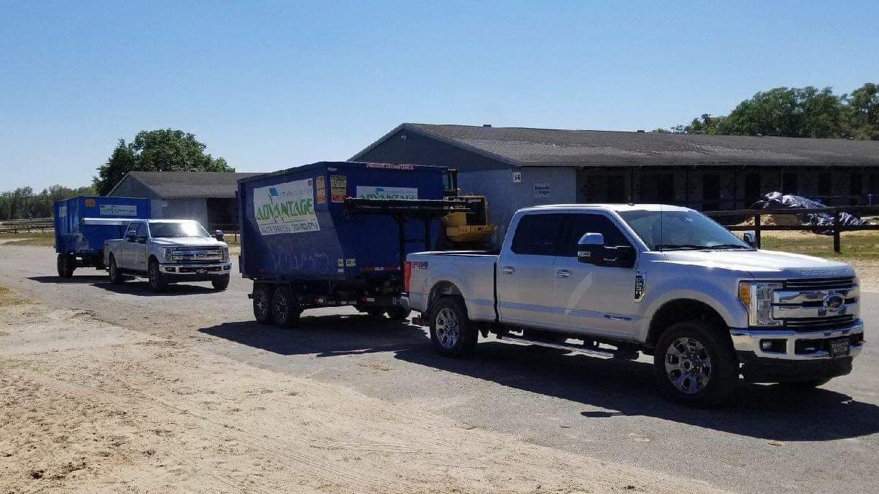 A white truck is pulling a blue trailer on a dirt road.