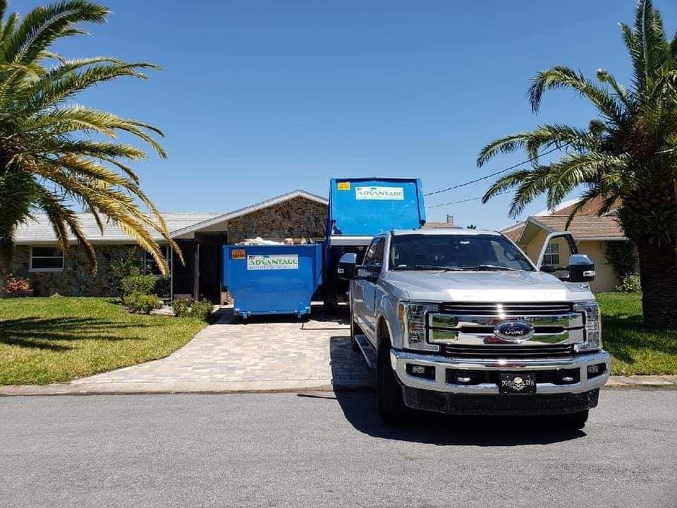 A truck is parked in front of a house with a dumpster in the driveway.