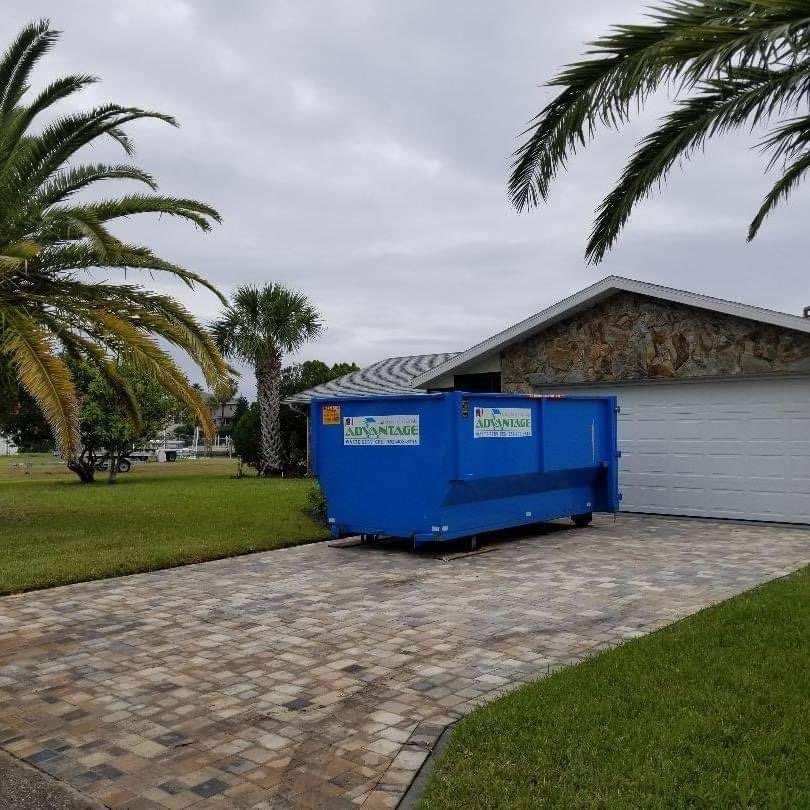 A blue dumpster is parked in front of a house