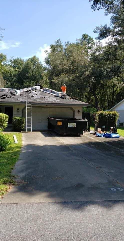 A house with a dumpster in front of it and a ladder on the roof.