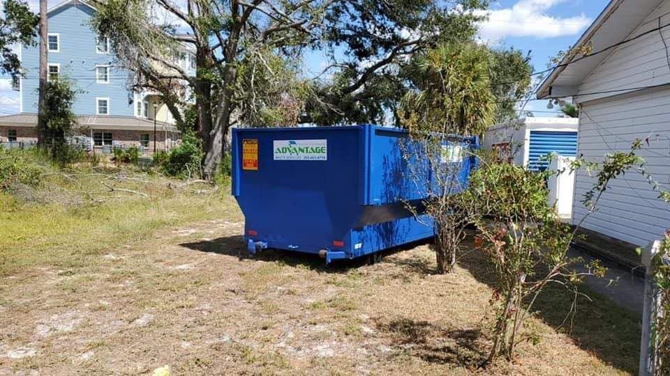 A blue dumpster is parked in a yard next to a house.