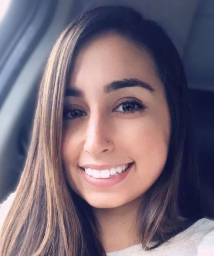 Smiling woman with long brown hair sitting in a car, wearing a light sweater.