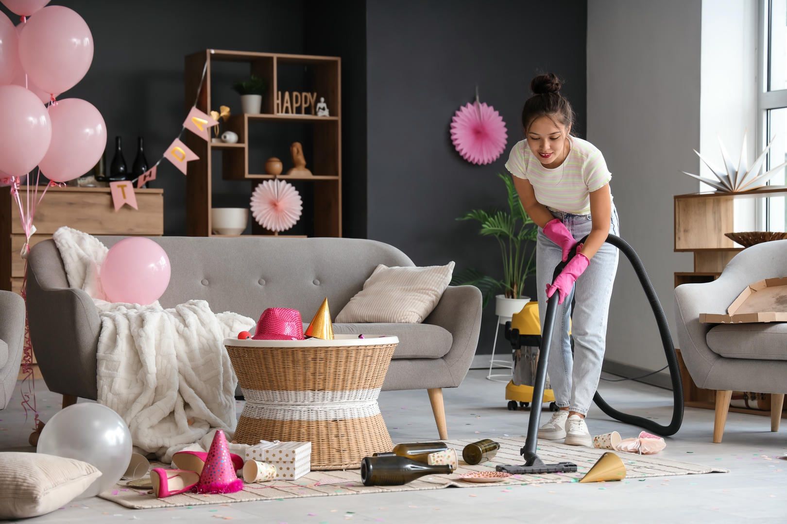 A woman is using a vacuum cleaner to clean a messy living room.