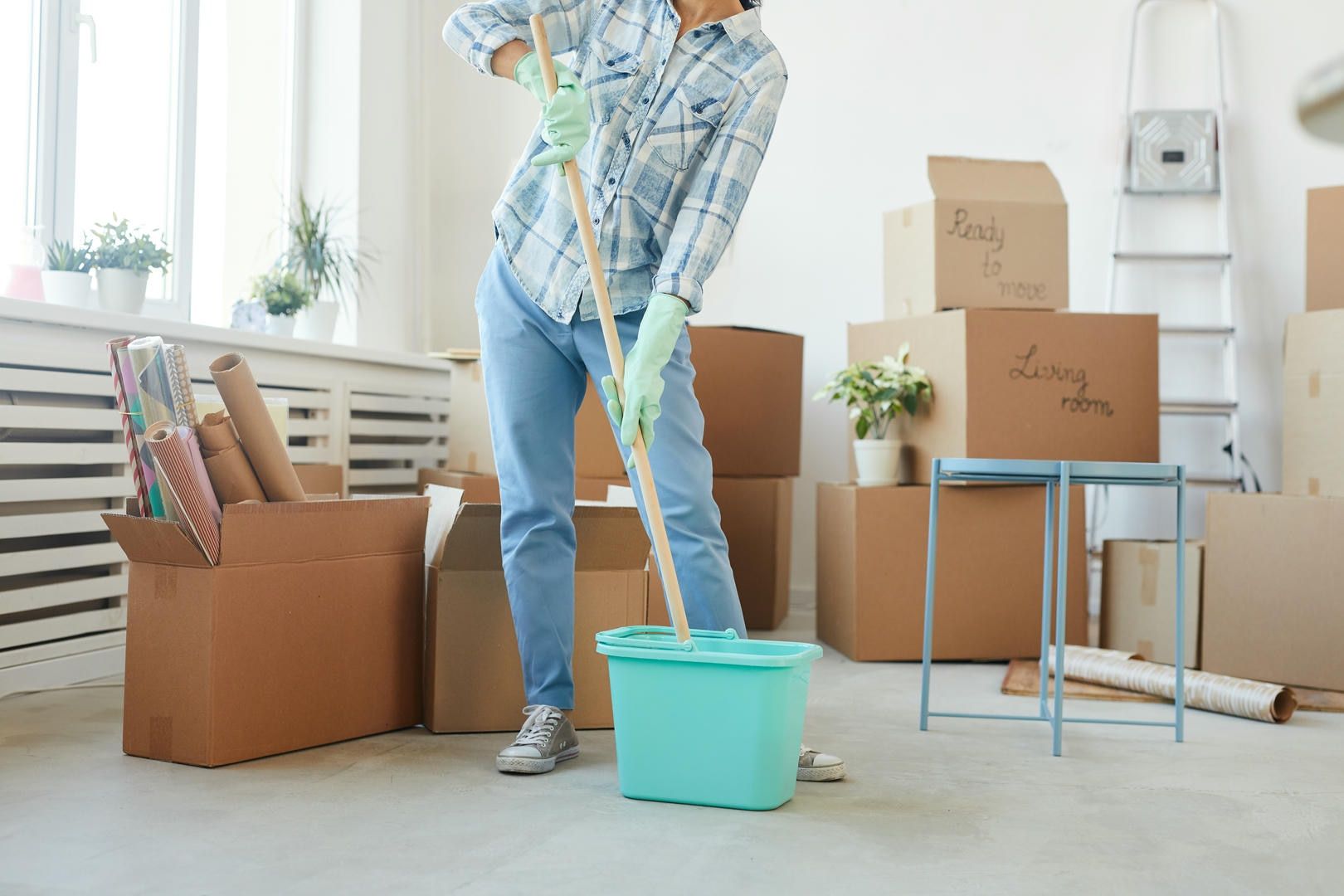 A woman is mopping the floor in a room filled with cardboard boxes.