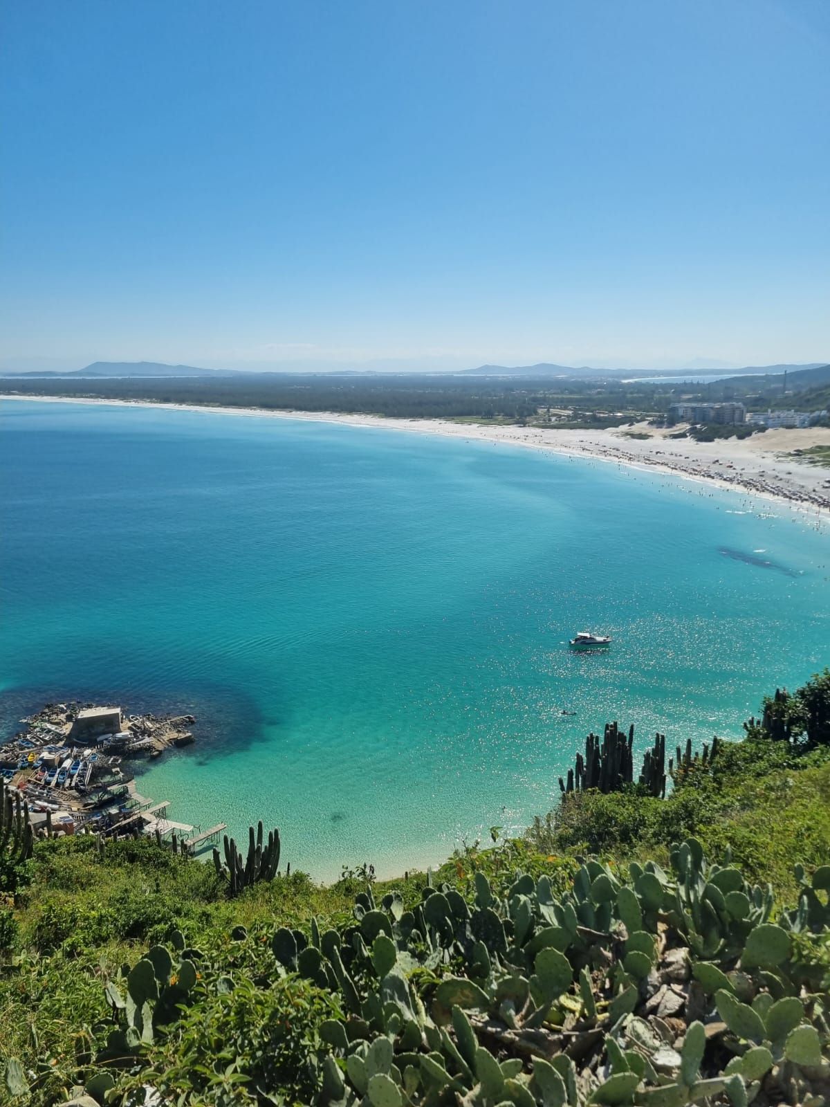 Baía de um azul turquesa vibrante, praia de areia branca e céu azul vistos de um mirante na encosta.