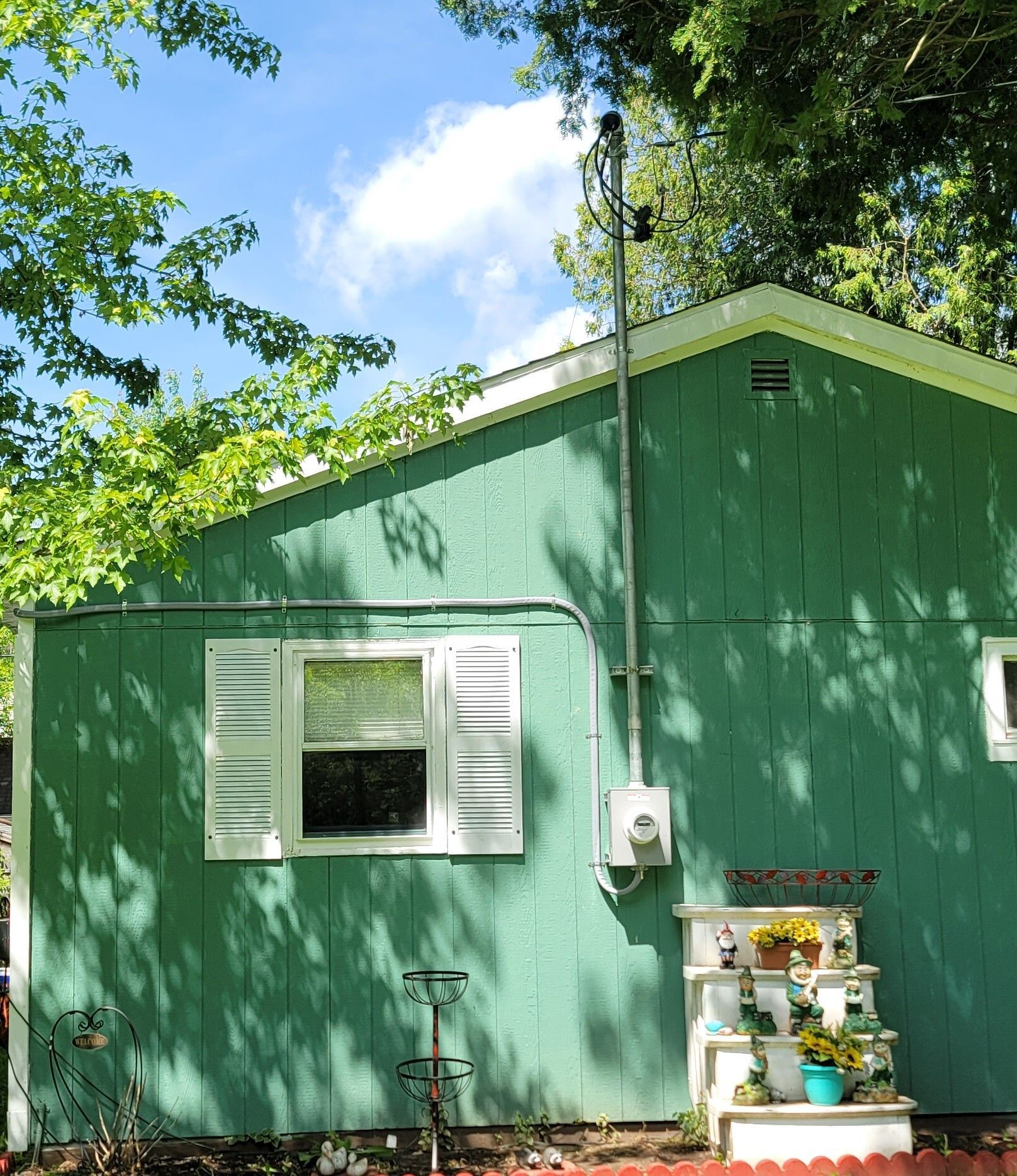Green house with new electrical 200A service running up side; window, display shelf, and sky visible.