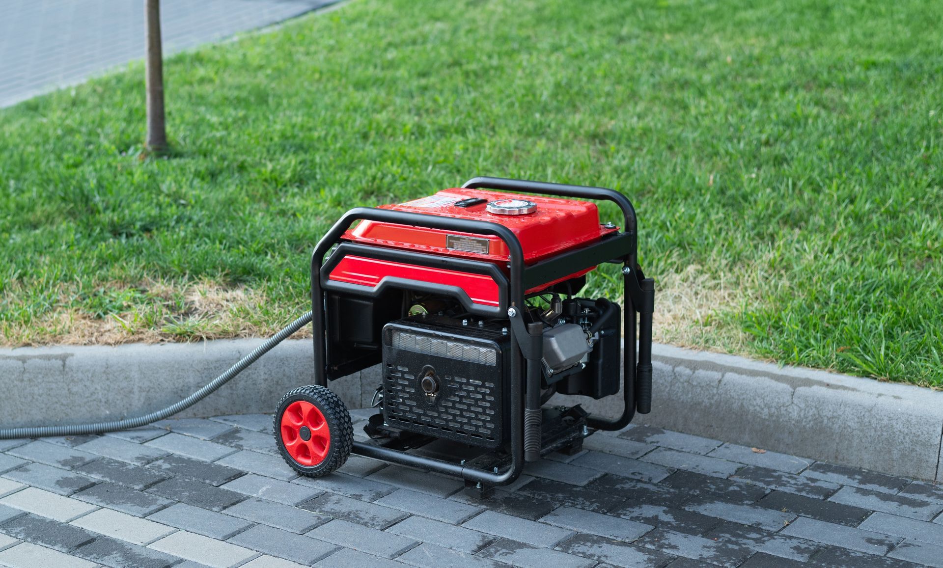 Red and black portable generator with a hose, on a paved surface next to grass.