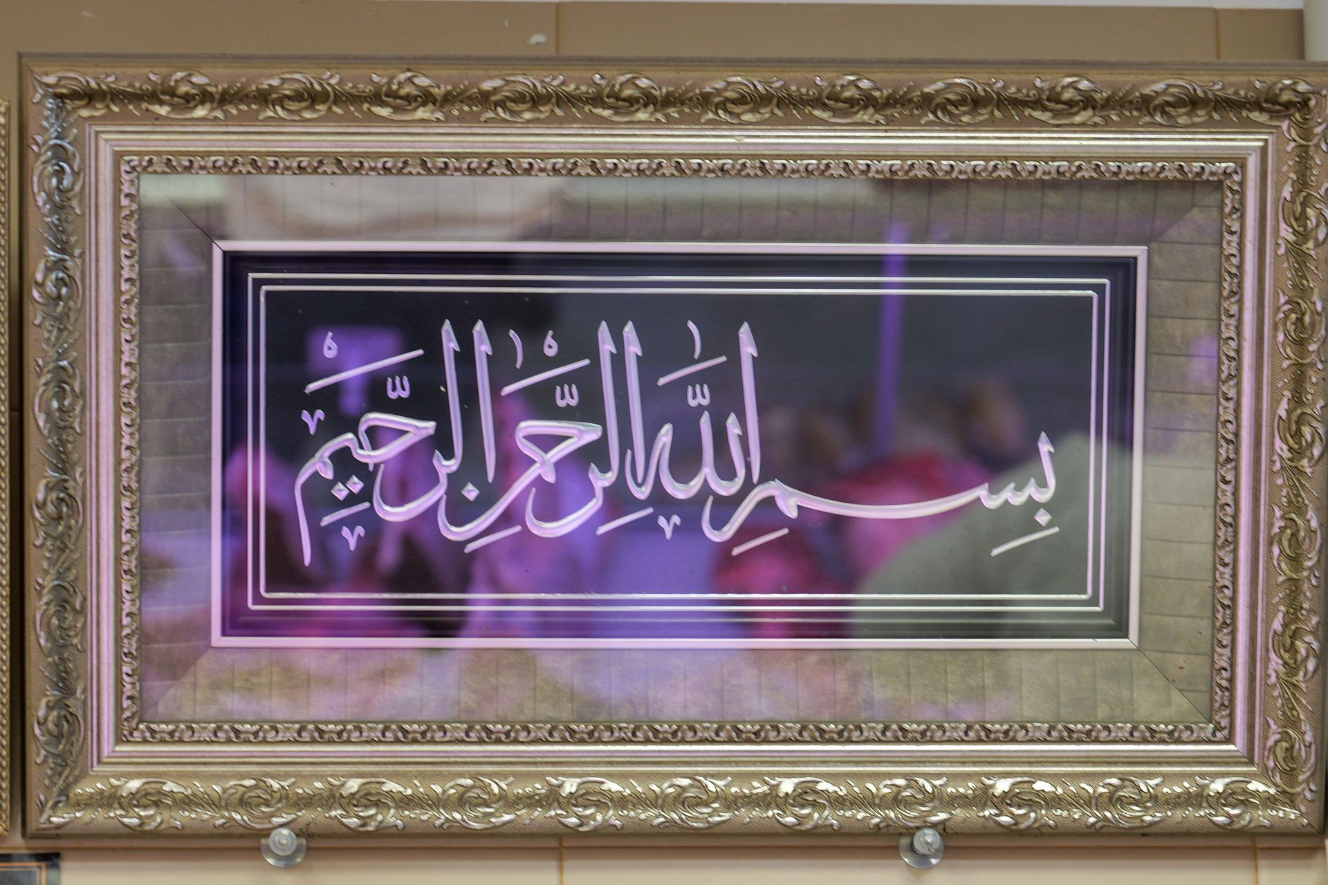 Opera d'arte incorniciata con calligrafia araba nei toni dell'oro e dell'argento con accenti viola e la frase 