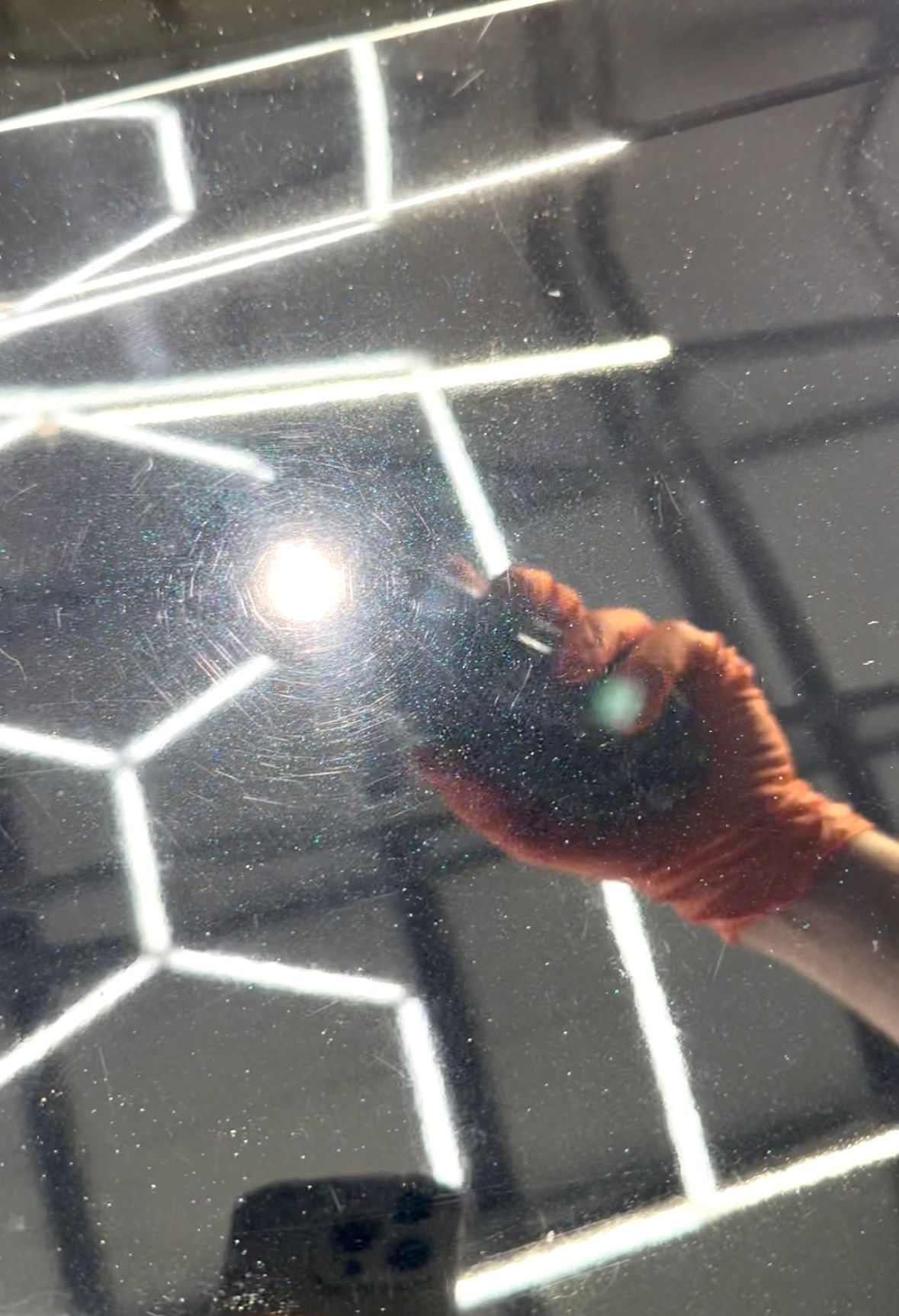 Person with orange glove polishing a car, reflection of shop lights visible.