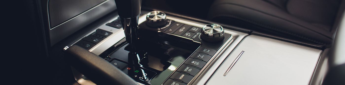 A high-angle view of a modern luxury car's center console featuring a gear shifter, control knobs, and trim buttons.