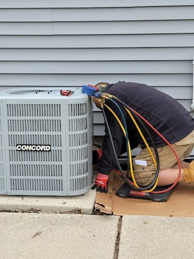 A man is kneeling down next to a concord air conditioner.