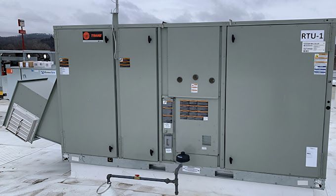 A large air conditioner is sitting on top of a snow covered roof.