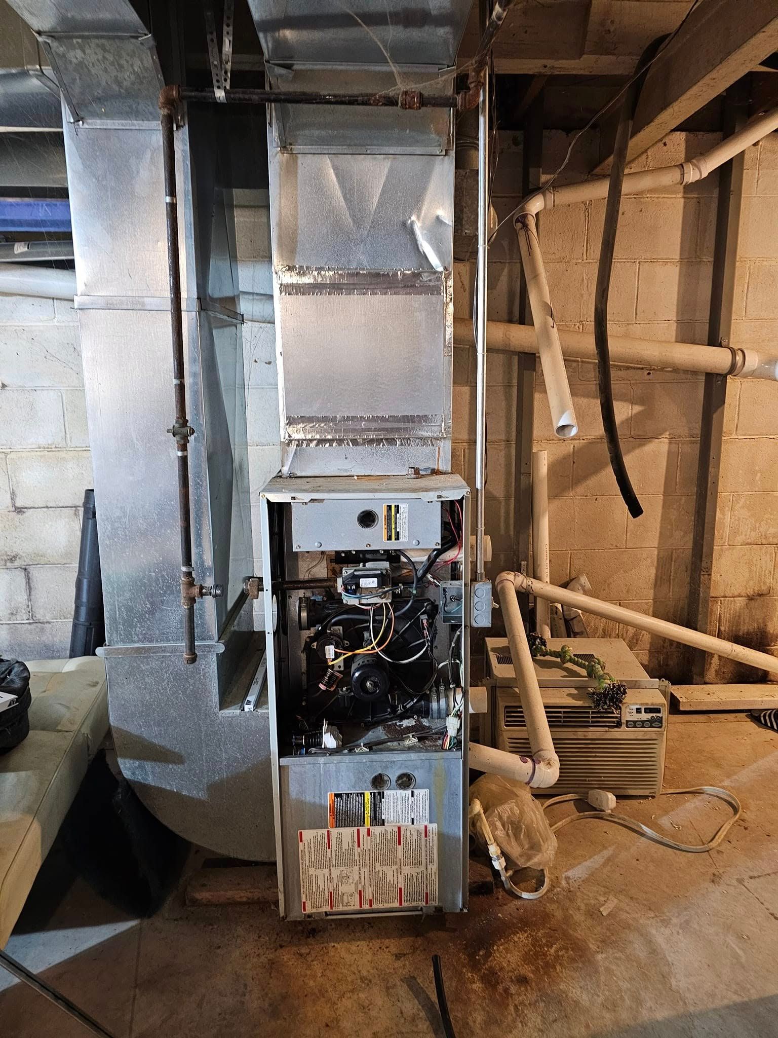 A furnace is sitting in a basement next to a brick wall.