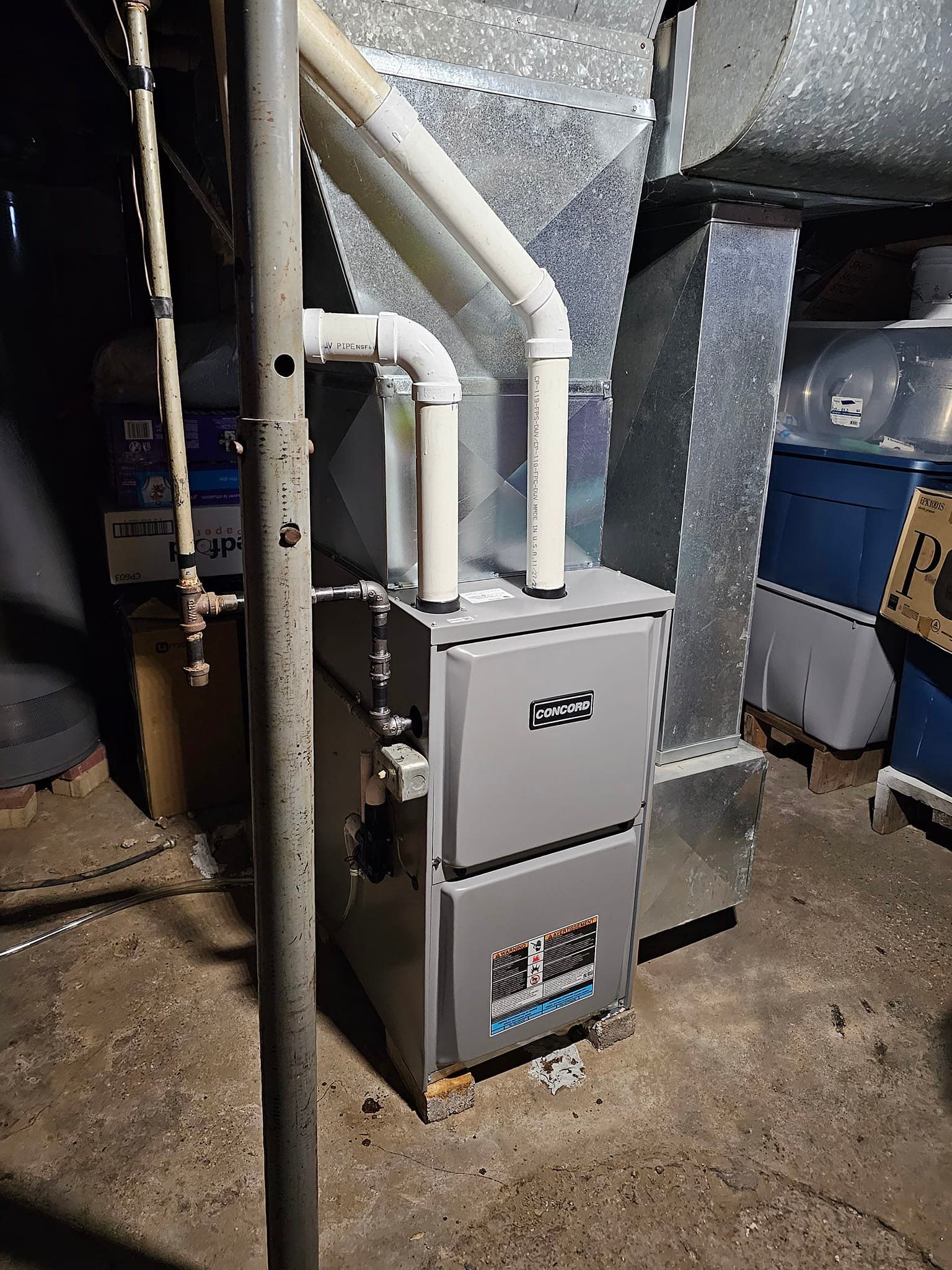 A furnace is sitting in a basement next to a pipe.