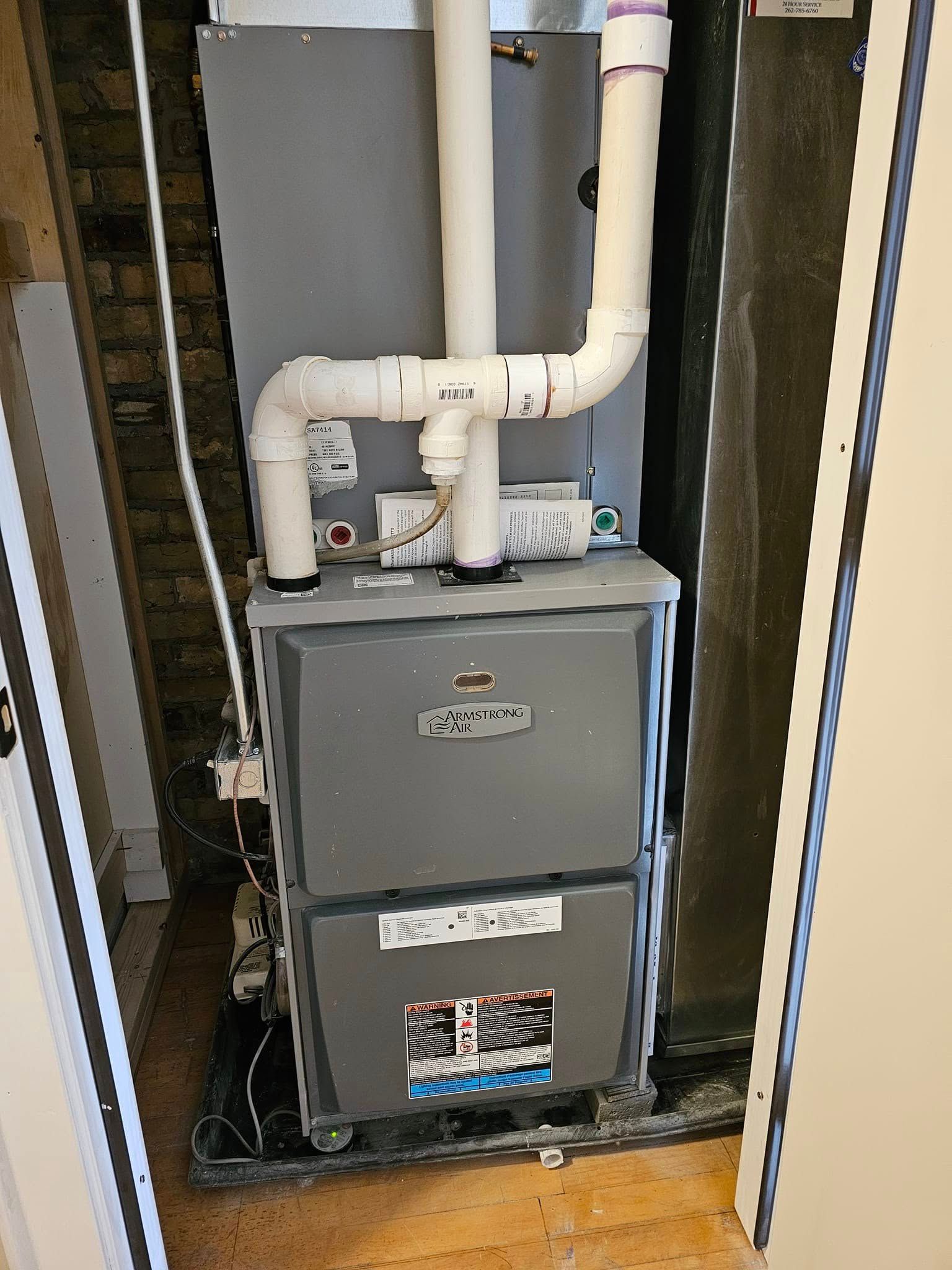 A furnace is sitting in a corner of a room next to a door.