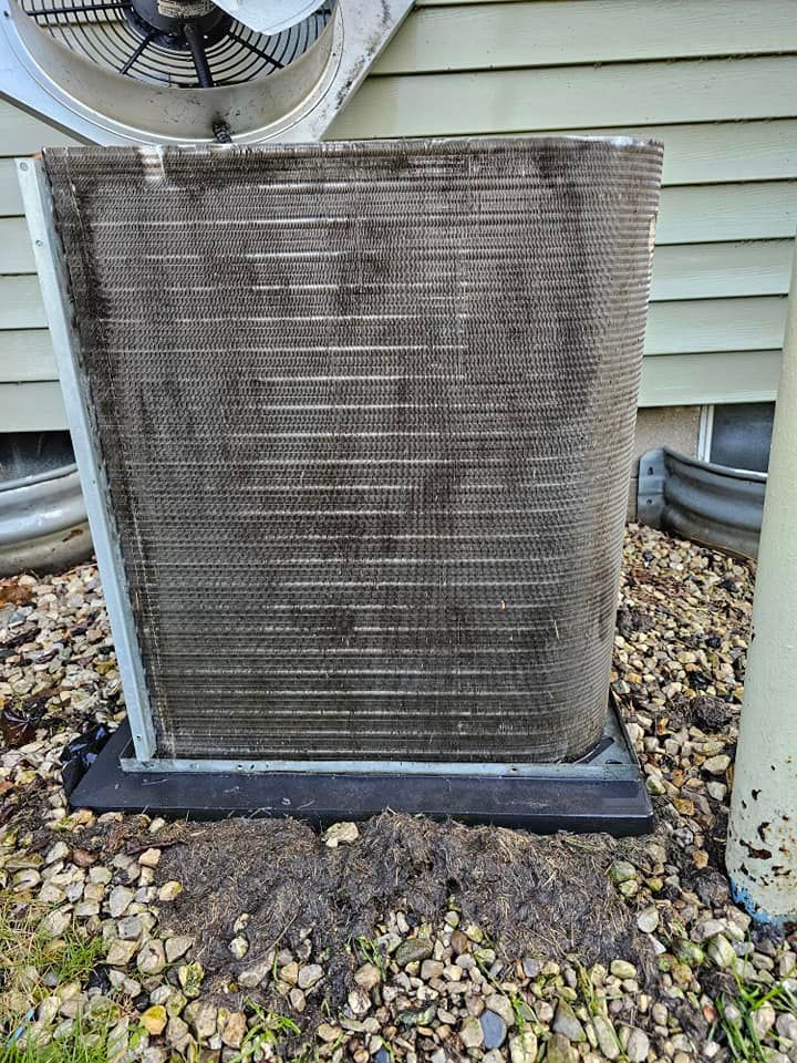 A dirty air conditioner is sitting on the ground next to a house.