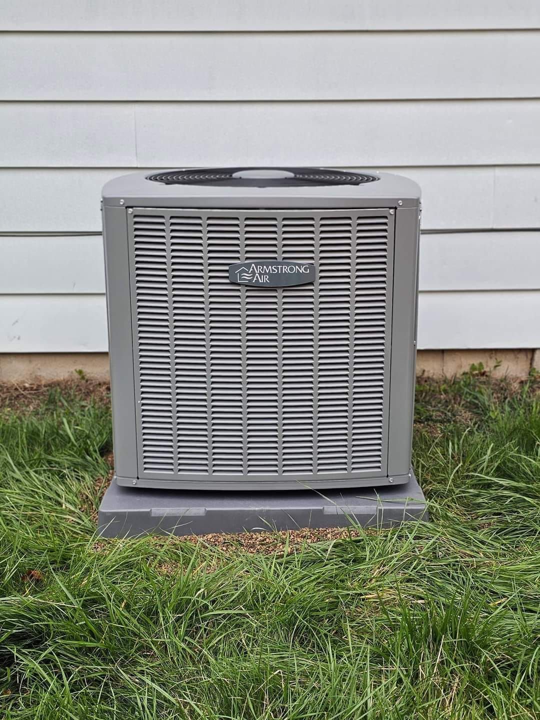 An air conditioner is sitting in the grass in front of a house.