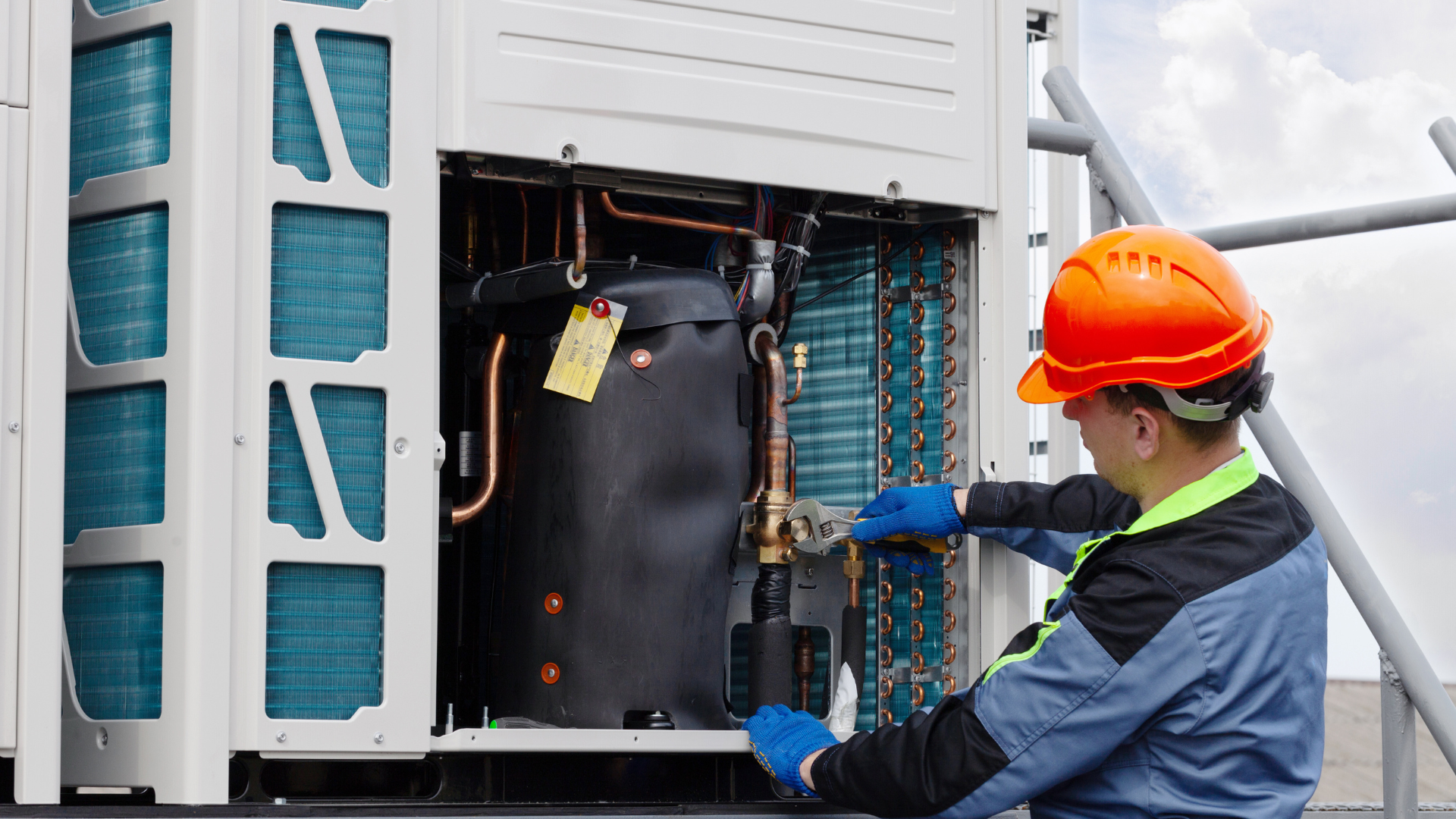 A man wearing a hard hat is working on an air conditioner.