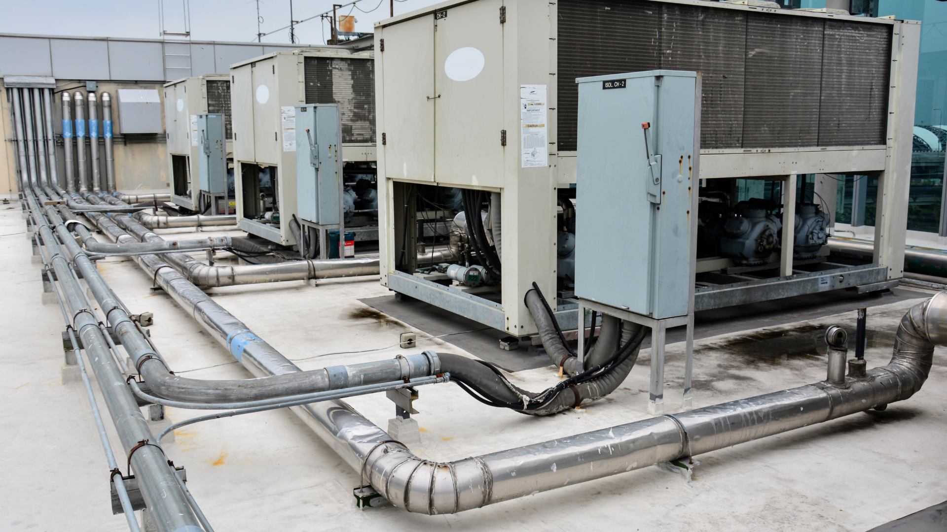 A row of air conditioners and pipes on the roof of a building.