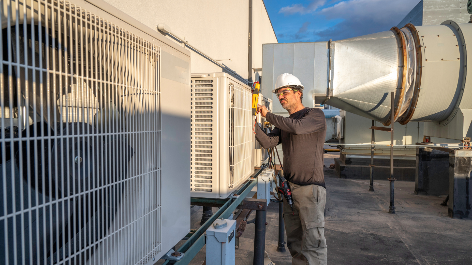 A man is working on an air conditioner on the roof of a building.