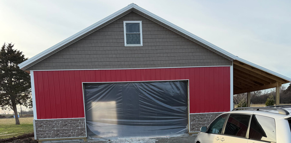 Construction of a wooden framed barn with a partially completed metal roof. Workers are installing walls.