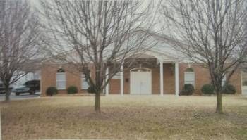 Brick building with white columns and leafless trees in front, seen across a grassy lawn.