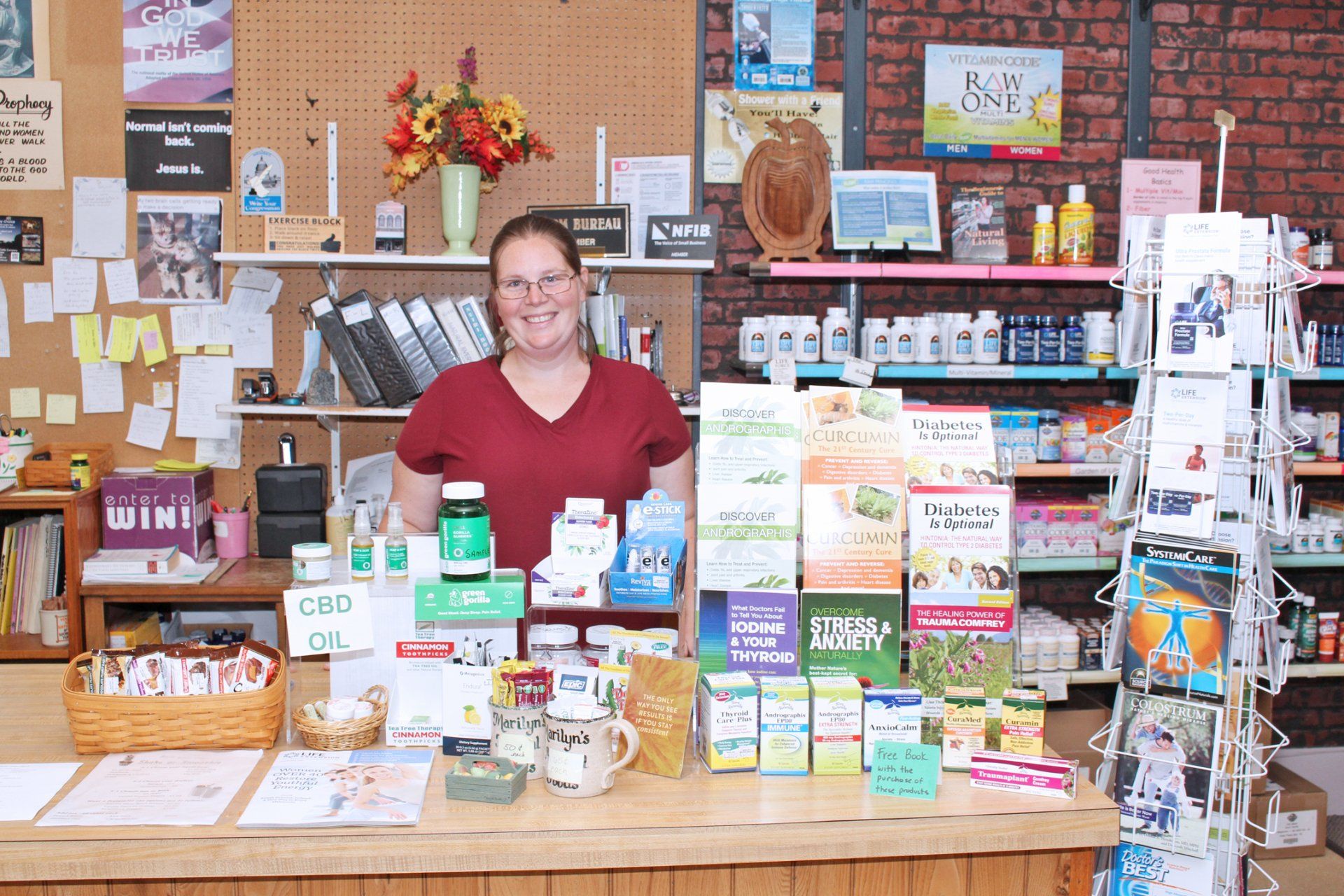 A person smiling behind a store counter filled with various supplements and pamphlets.