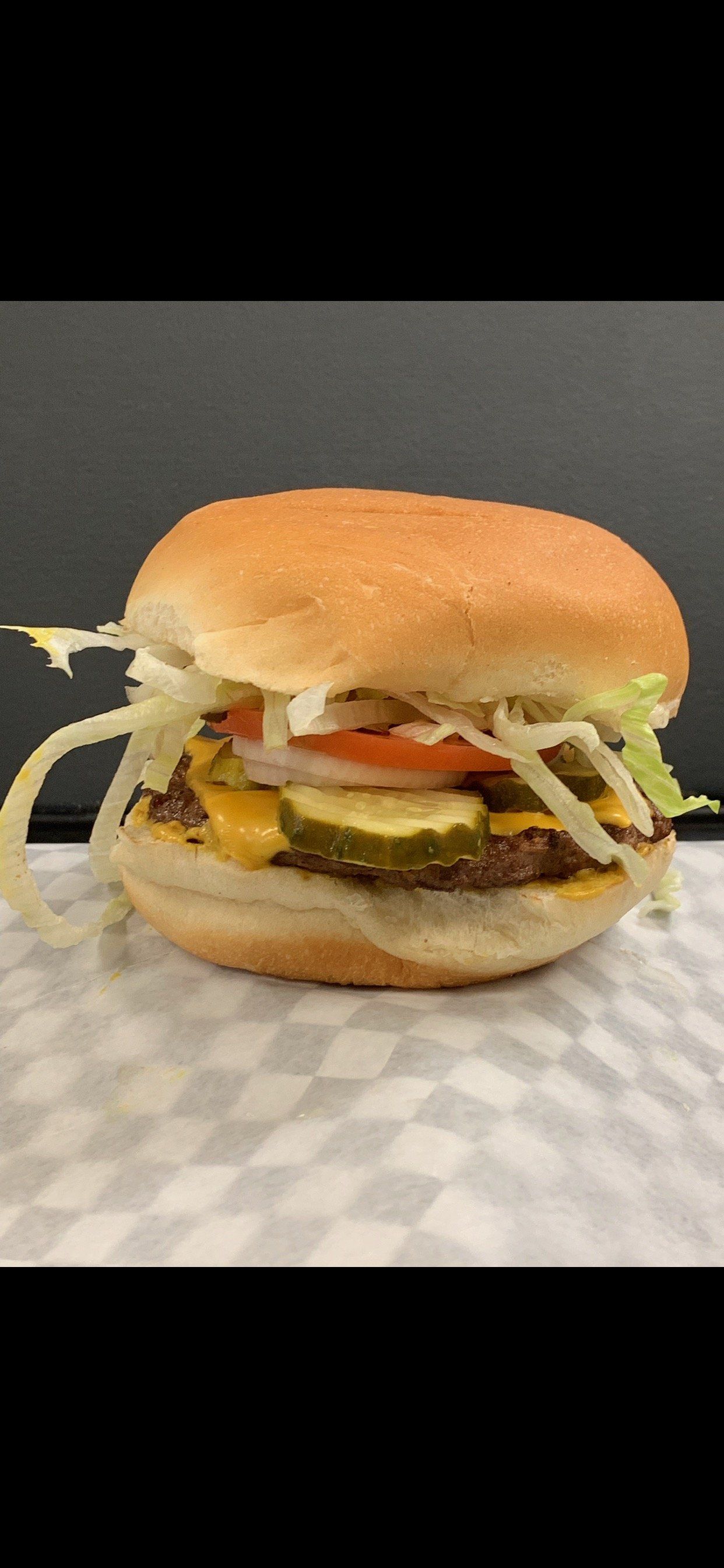 Burger with cheese, pickles, lettuce, and tomato on a checkered surface.