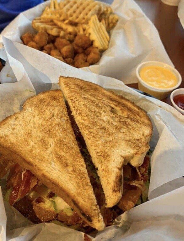 Toasted sandwich with bacon, waffle fries, tater tots, and dipping sauces on a table.
