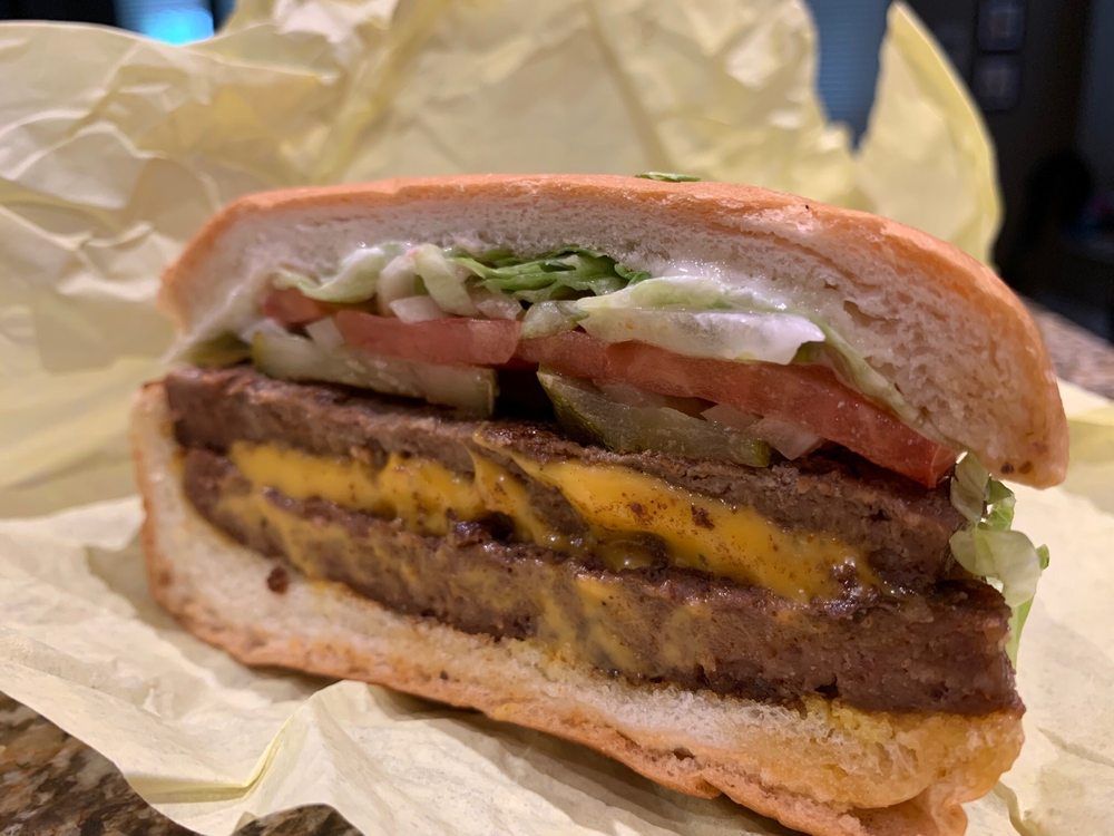 A sliced cheeseburger with two patties, cheese, tomato, lettuce, and pickles on a toasted bun.