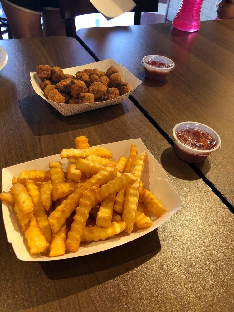 Crinkle-cut fries and popcorn chicken in paper trays with ketchup cups on a wooden table.