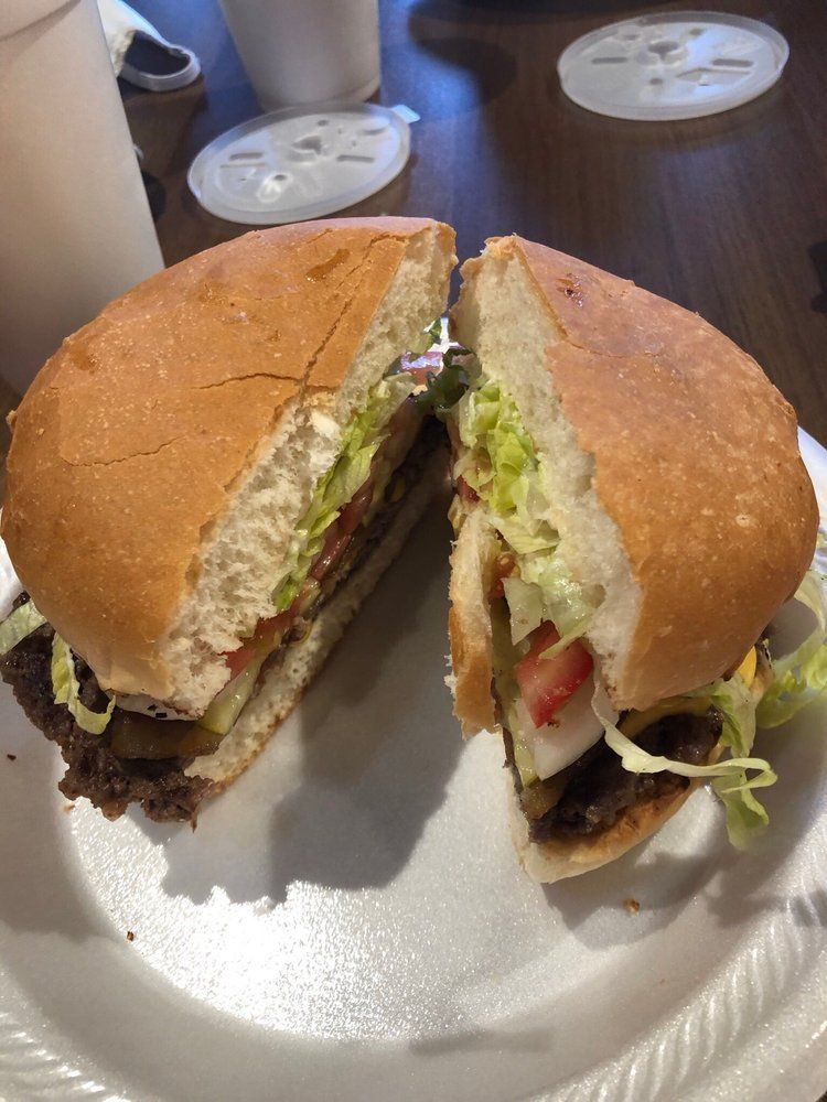Burger cut in half on a white plate, showing a beef patty, lettuce, tomato, and pickles.