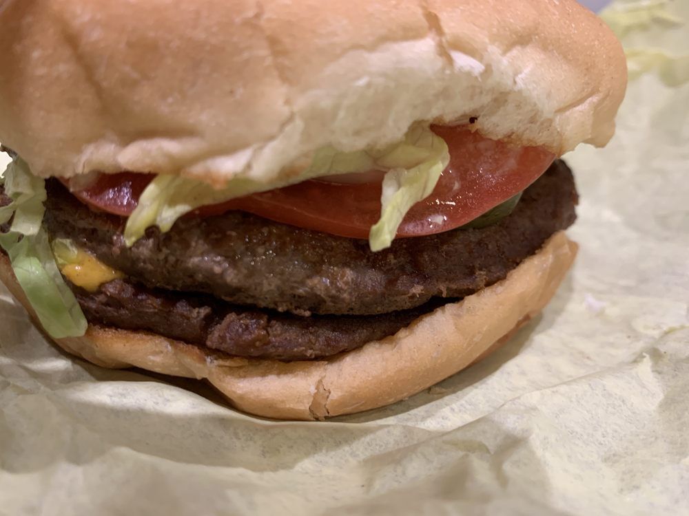 Double-patty burger with lettuce, tomato, and cheese on a bun, resting on yellow paper.
