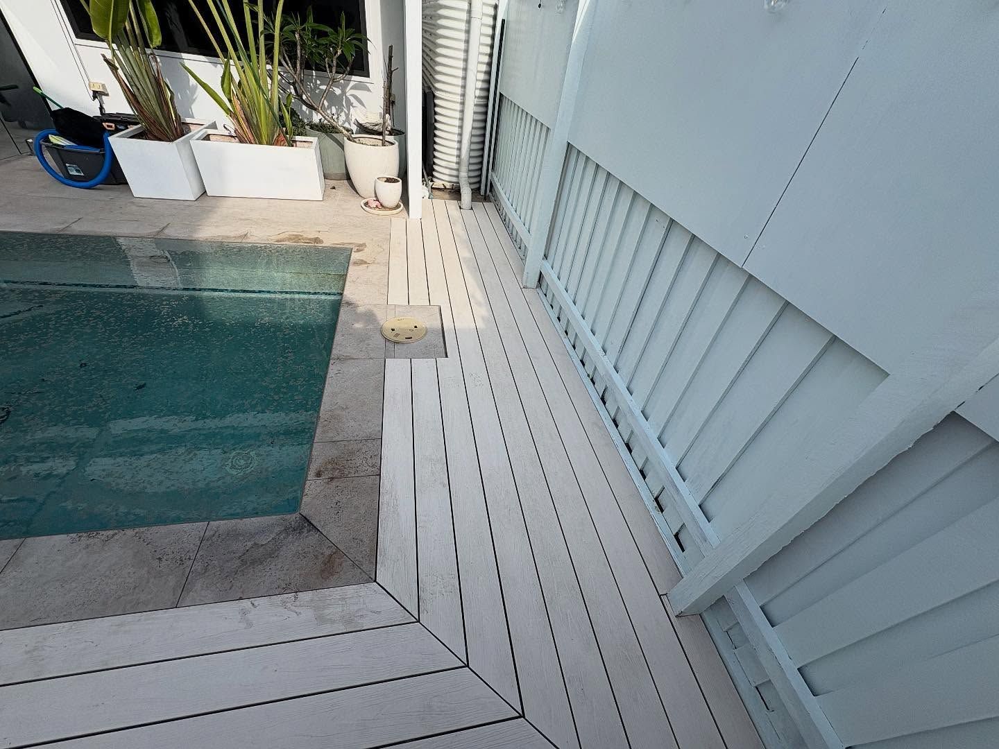 White deck beside a turquoise pool, with potted plants and a small step down to the water