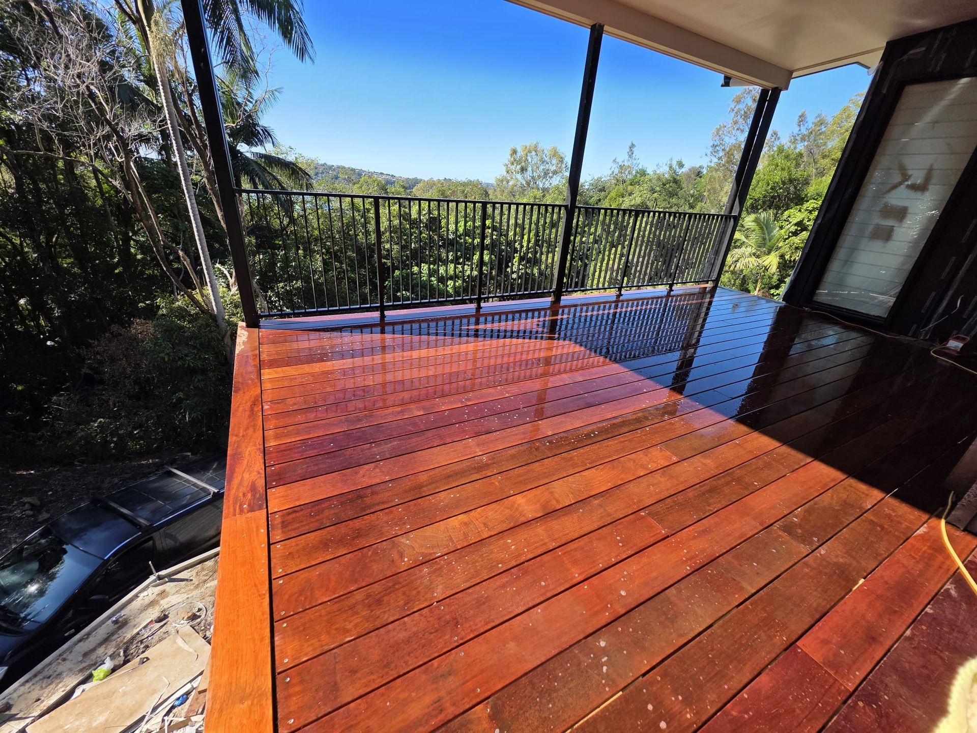 Small backyard patio with wooden deck, green turf, glass sliding doors, and tools on the floor