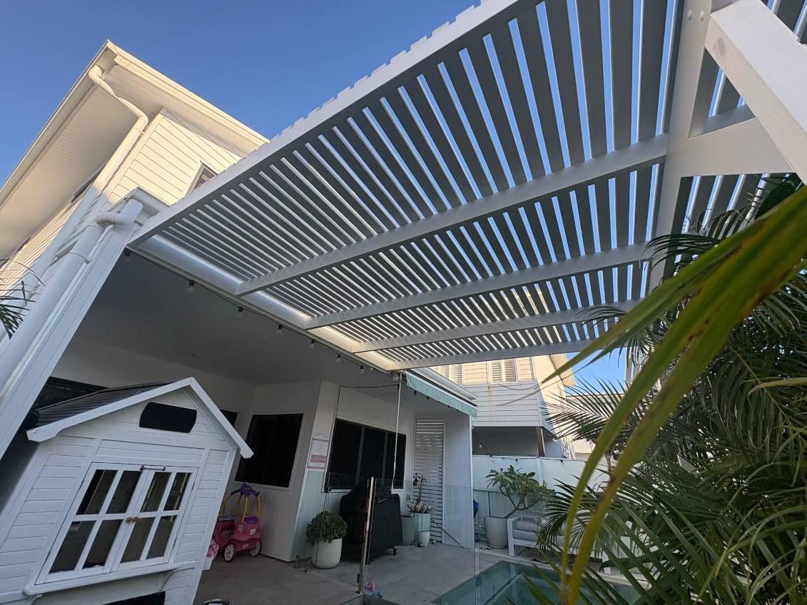 White pergola beside a turquoise pool, with a white fence and potted tree in a backyard patio area