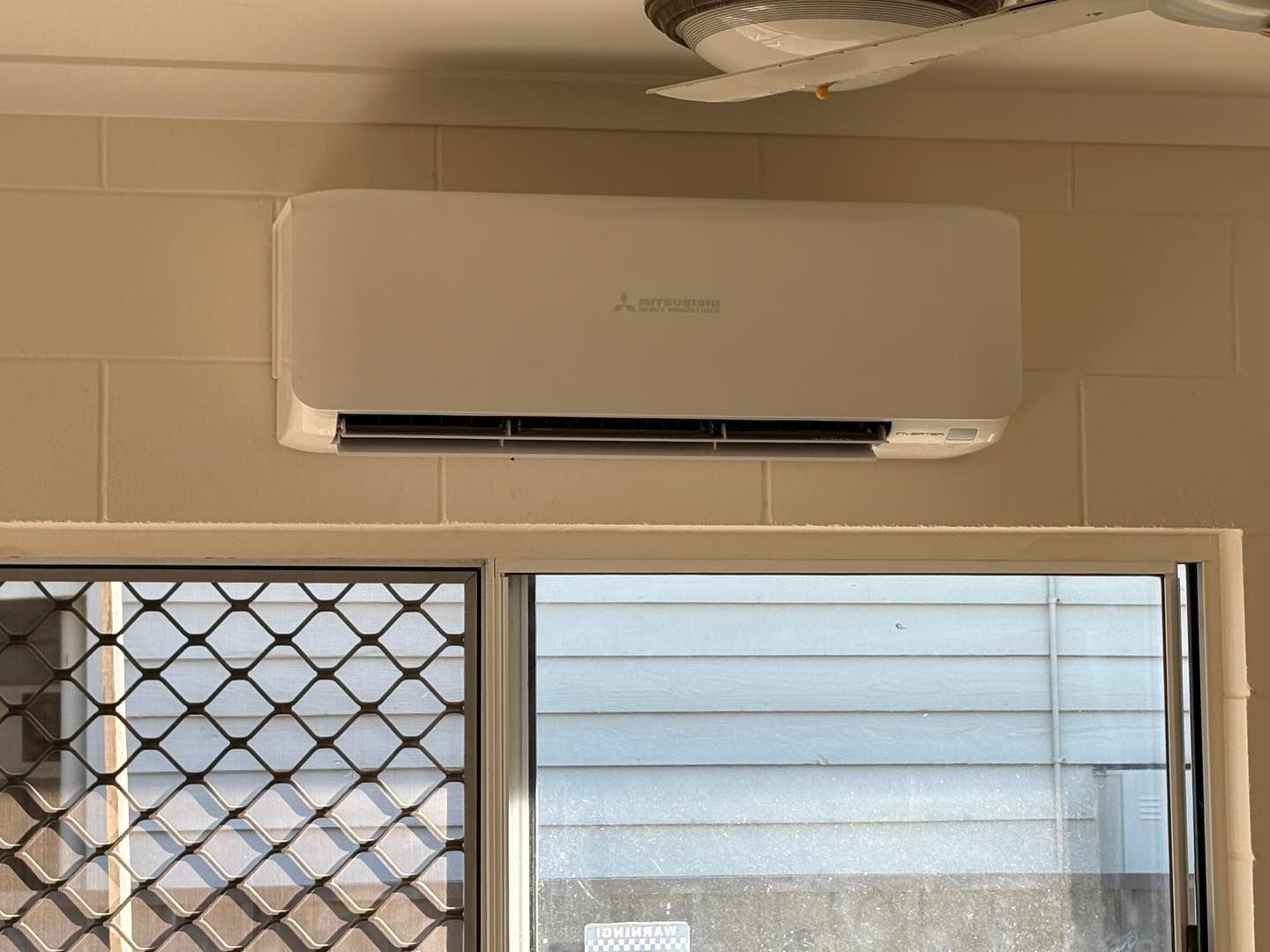 White Air Conditioning Unit Above a Window With Security Bars — JPower Energy in Kamerunga, QLD