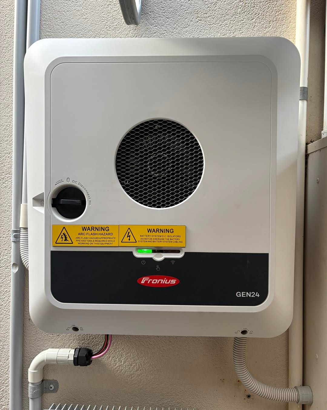 A Wall-mounted Fronius Solar Inverter With A Grey Casing, A Circular Fan Vent, And A Green Power Indicator Light  — JPower Energy in Kamerunga, QLD