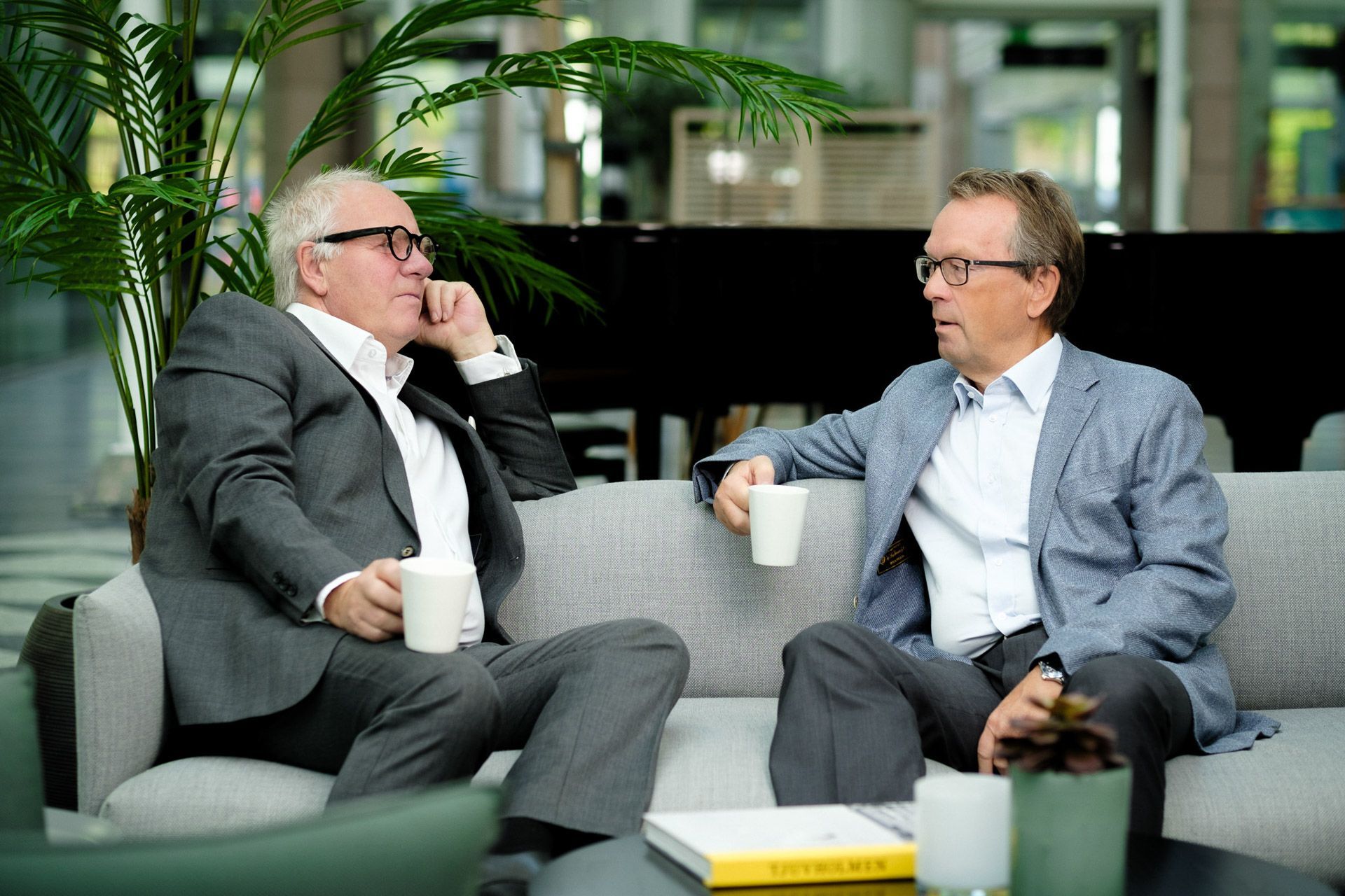 To menn i dress sitter på en sofa og snakker med hverandre.