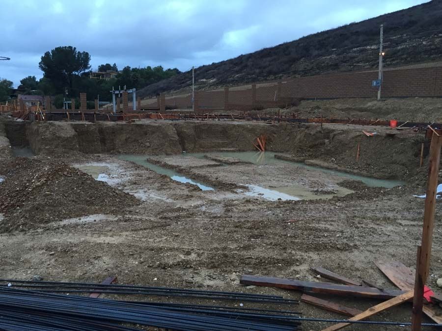 Construction site with freshly dug foundations; muddy ground, hill in the background.
