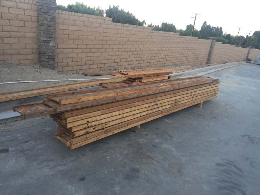 Stack of wooden planks on asphalt near a brick wall.
