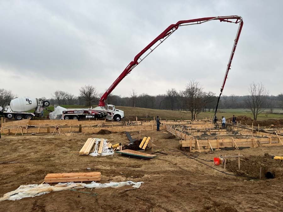 Concrete being poured into wooden forms at a construction site on a cloudy day.