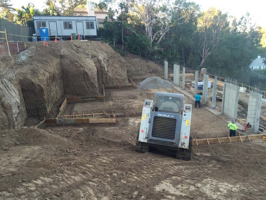 Construction site with a bobcat, concrete forms, and workers building a foundation.
