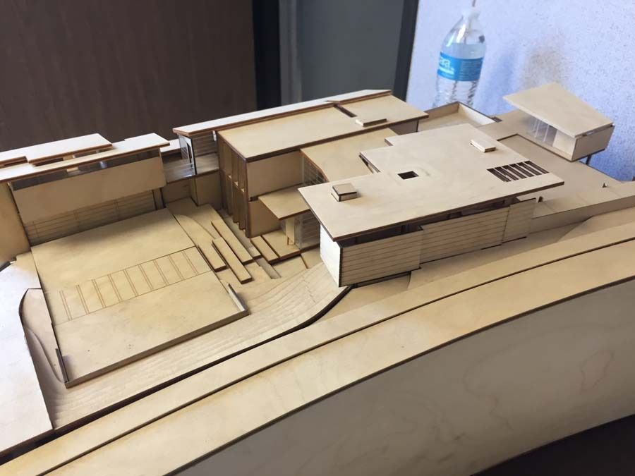 Architectural model of a multi-level building made of light-colored wood, set on a contoured base.