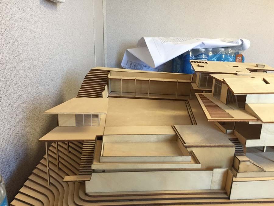 Architectural model of a house with a pool and terraced landscape, made of light wood.