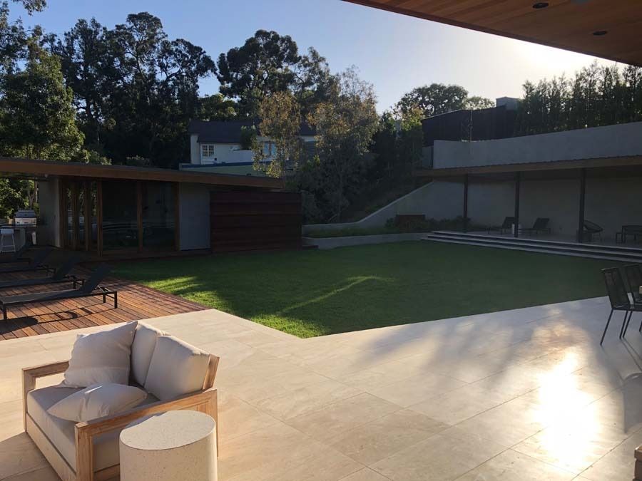Patio with a cream sofa, grass, and a modern house with a sloped roof. Sunny outdoor scene.